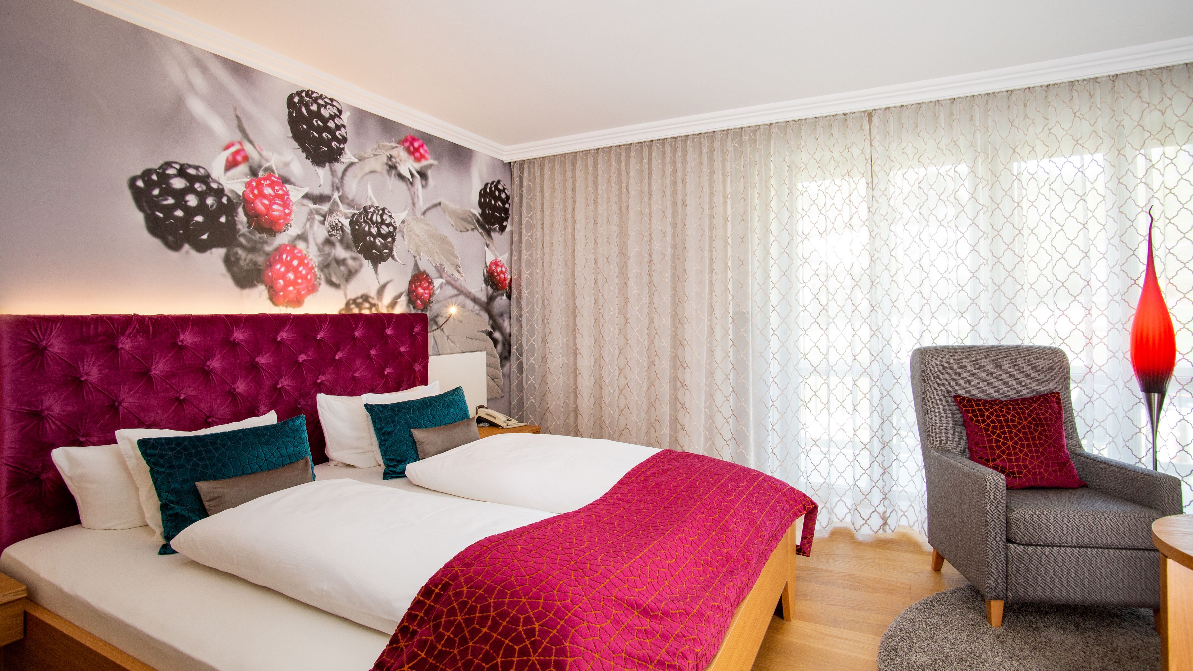 Una habitación de hotel moderna con una cama grande, un sillón gris y una lámpara roja decorativa.