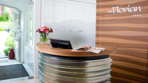 A reception desk with a wooden finish and a glass panel, a vase with flowers, and a sign that reads "St. Florian" with a heart symbol and stars. - Hotel St Florian (Frauenau)