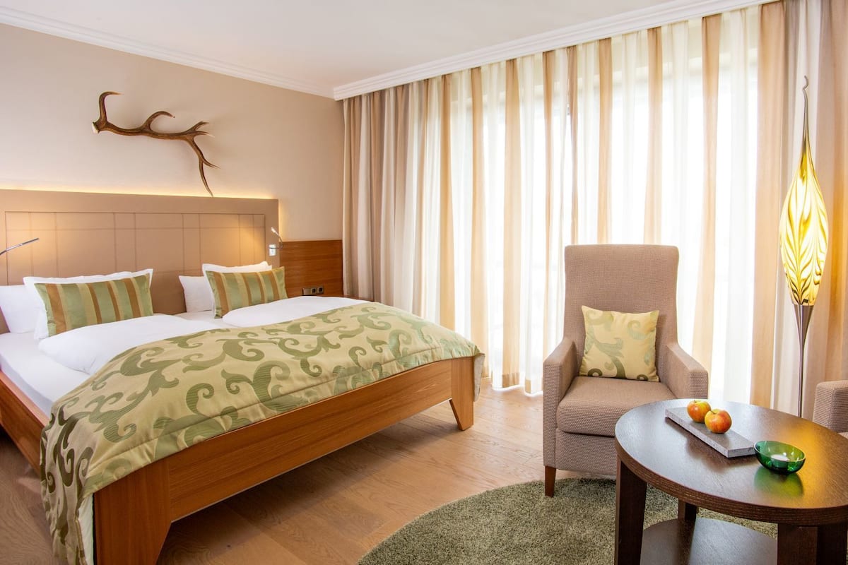 Habitación de hotel con una cama grande, una silla, una mesita con fruta y cortinas.