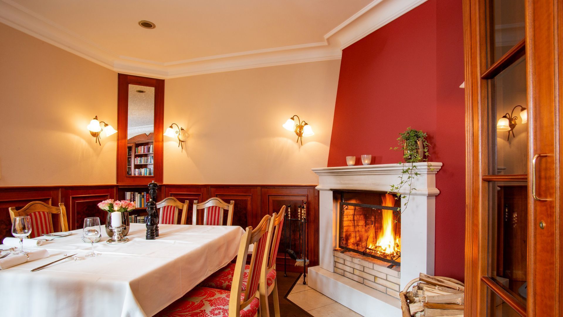 Comedor con chimenea, sillas de madera, una mesa lista para comer e iluminación en la pared.