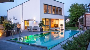 A modern hotel with a swimming pool, outdoor seating, and a well-lit entrance. - Hotel St Florian (Frauenau)