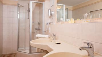 A bathroom with a glass-enclosed shower, a sink with a mirror, and toiletries on the countertop.