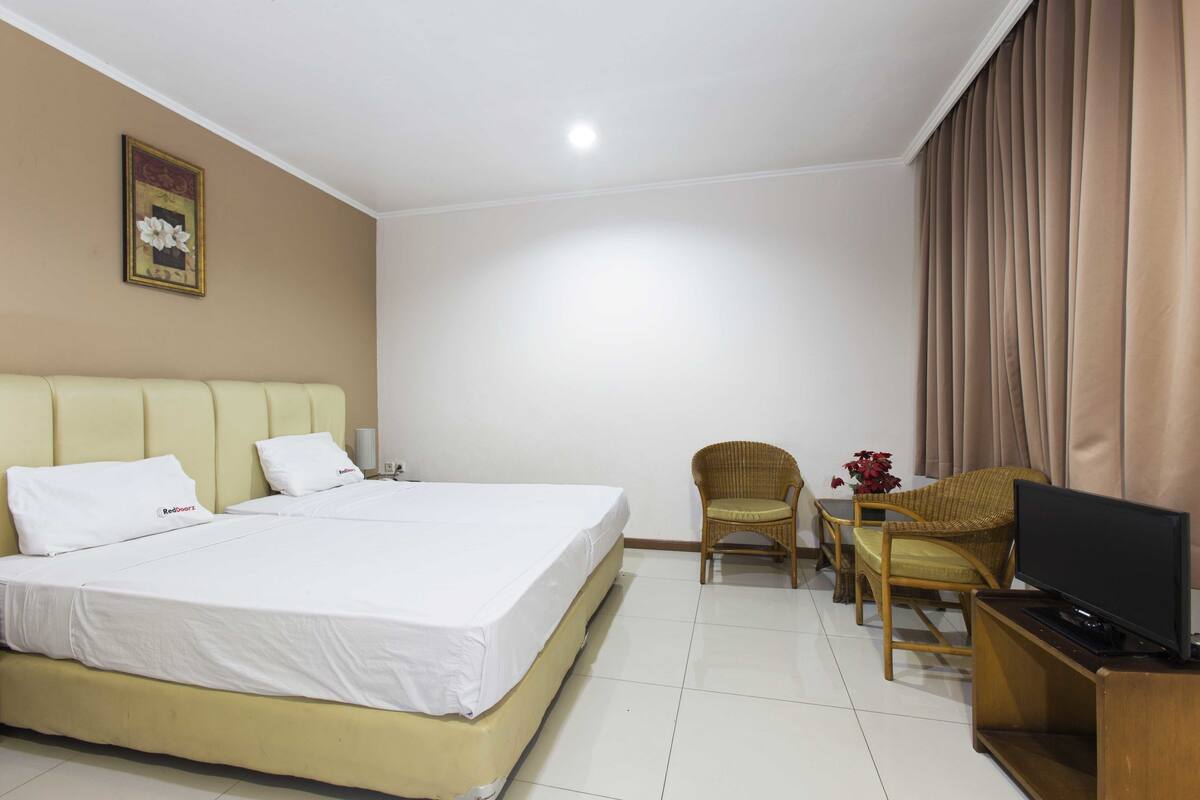 Una habitación de hotel con una cama grande, dos sillas, un televisor y una mesita.