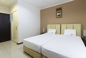 A double bed with white bedding, a beige headboard, and a nightstand with a lamp.