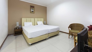 Habitación de hotel con cama doble, mesita de noche con lámpara, televisor y una silla de mimbre.