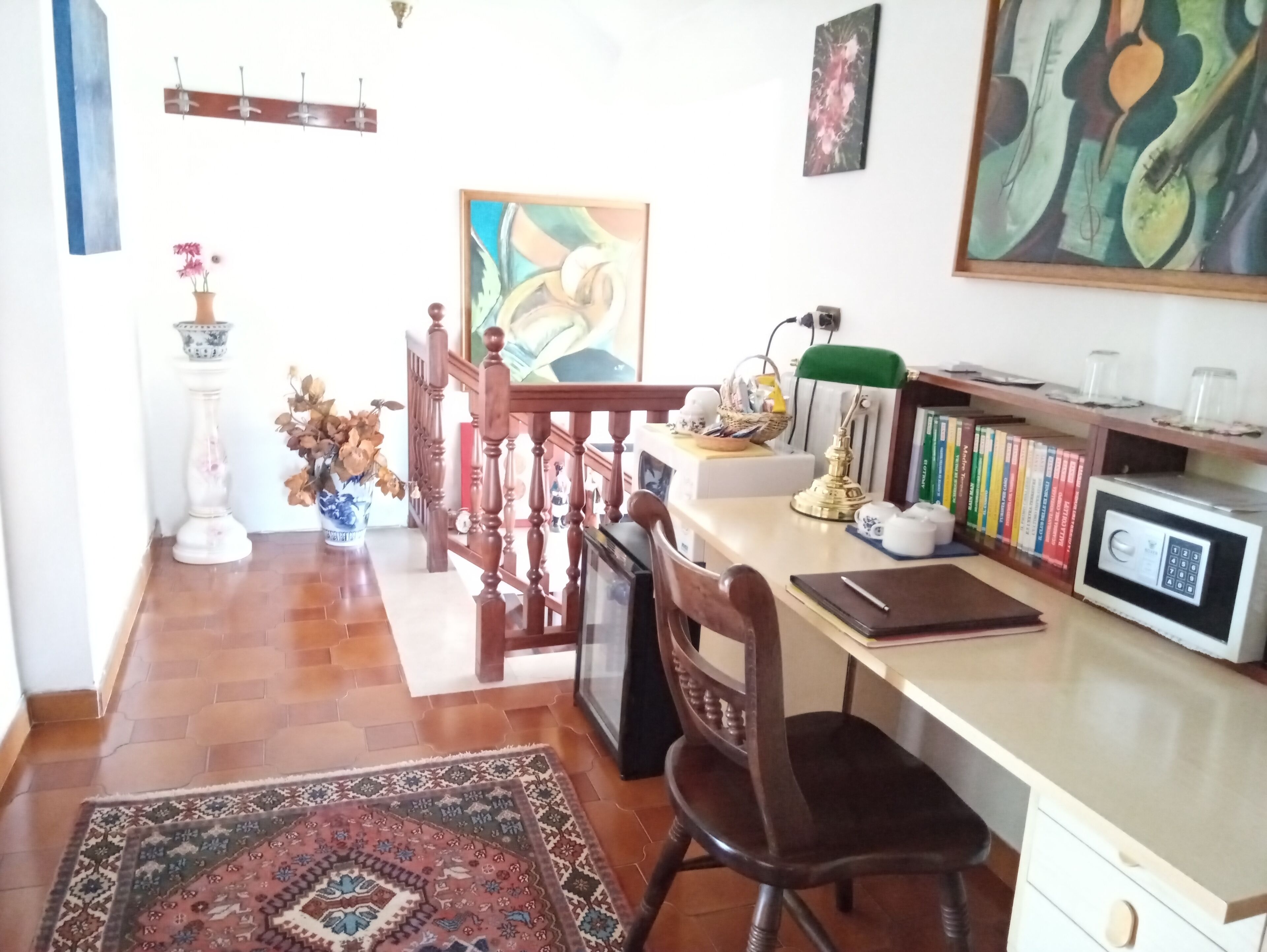 Une pièce bien éclairée, avec un bureau en bois, une chaise, une bibliothèque et un coin repas agrémenté d’un tapis à motifs.