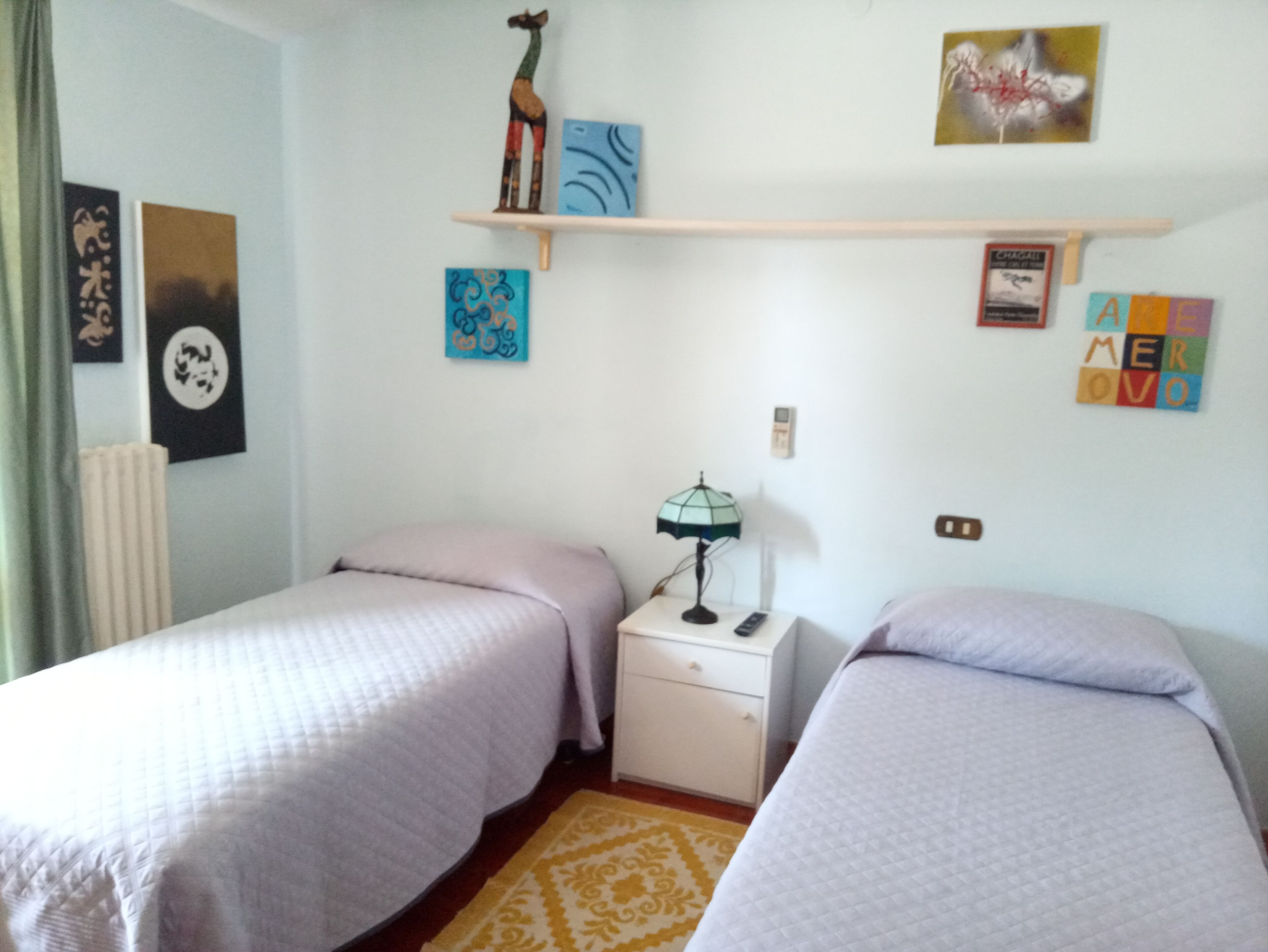 A bedroom with two beds, a nightstand, a lamp, and wall decorations.