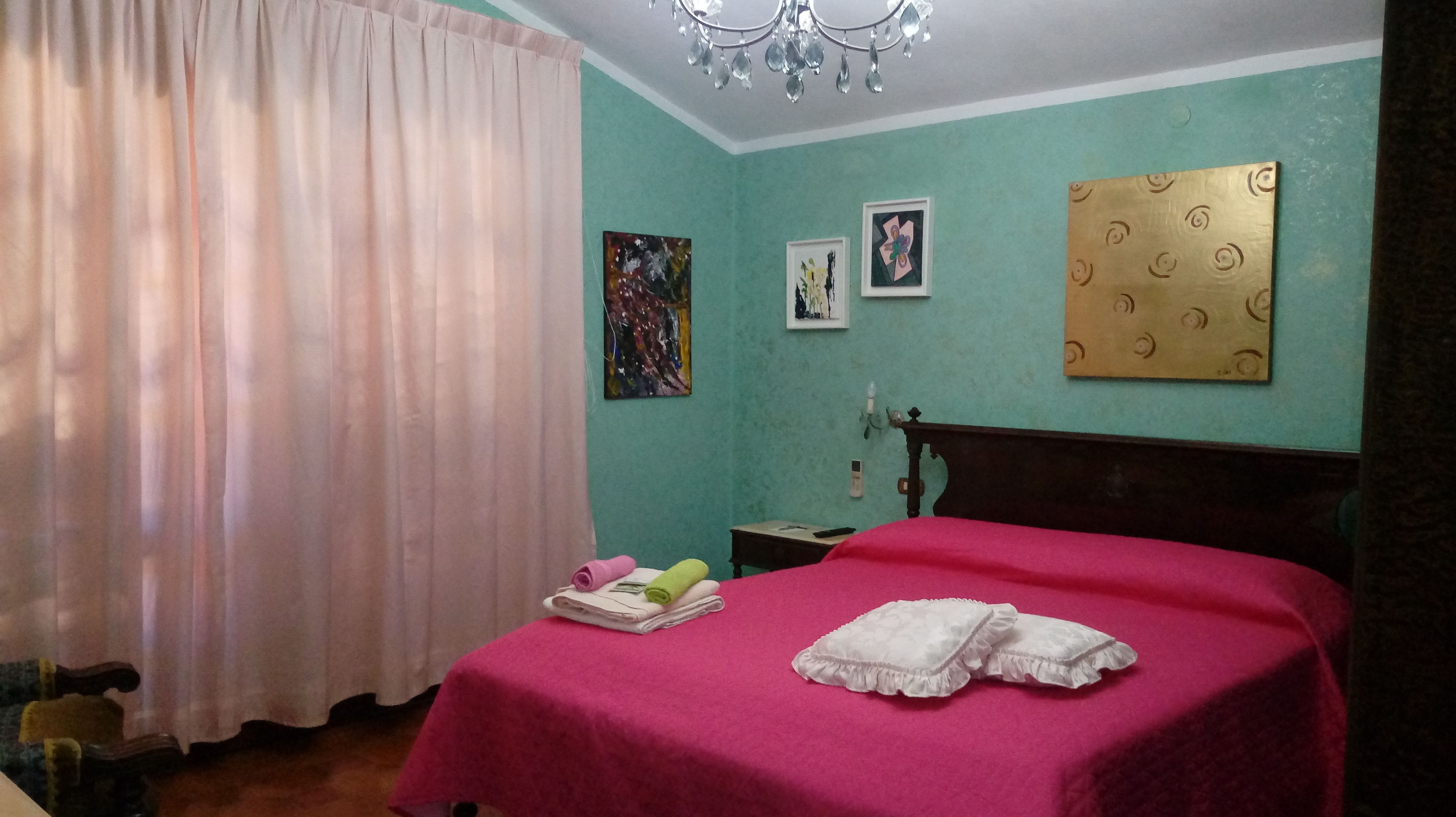 A room with a bed, a nightstand, a chair, a window with curtains, and wall art.