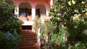 Um jardim que leva a um edifício com fachada rosa e janelas em arco.