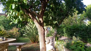 Um jardim com uma árvore, uma estátua de pedra e diversas plantas.