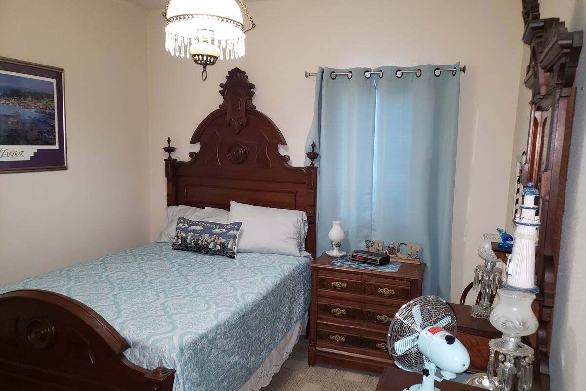 Een slaapkamer met een houten bed, een nachtkastje met een klok, een ventilator en een lamp.