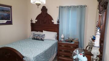 A bedroom with a wooden bed, a bedside table with a clock, a fan, and a lamp.