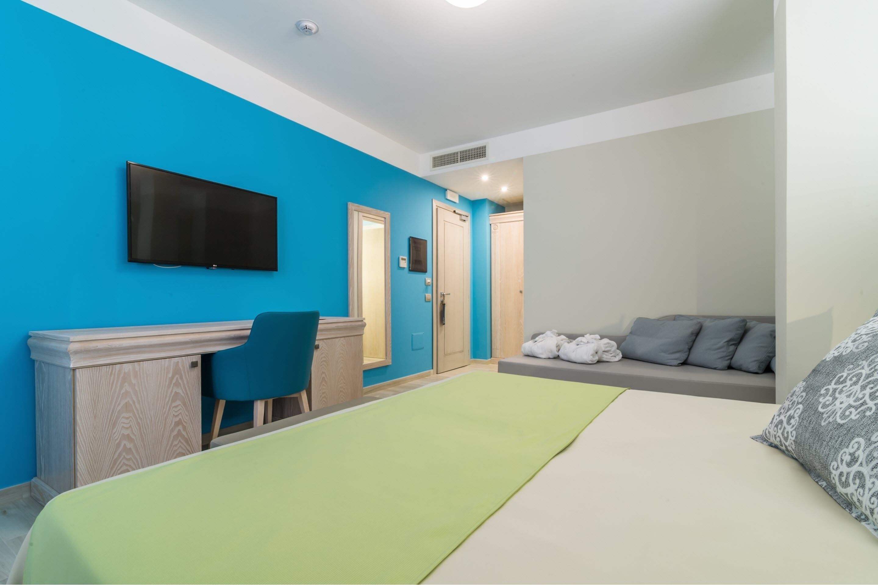 A bedroom with a bed, a desk, a chair, a TV, and a sofa.