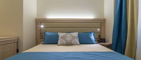 A neatly made bed with blue bedding and a decorative pillow, a bedside telephone, and a nightstand.
