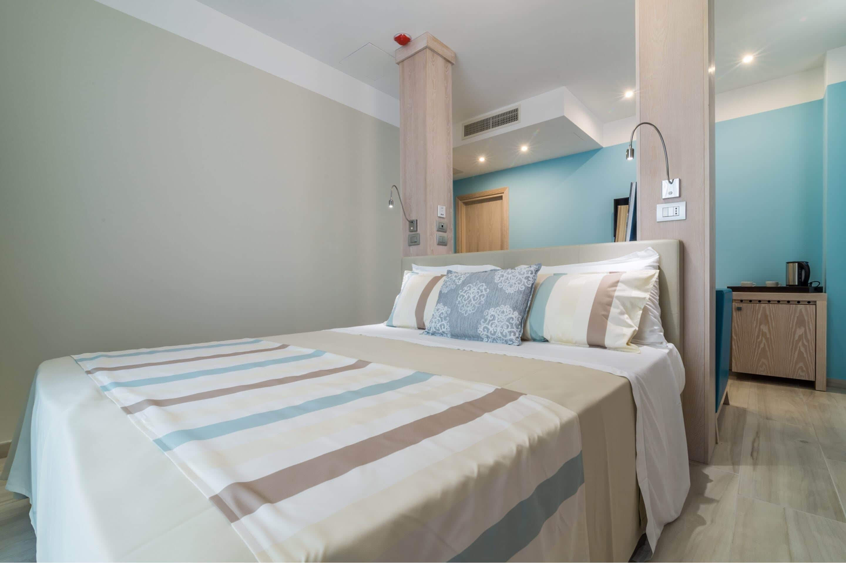Una habitación de hotel con una cama grande, una mesita de noche de madera y una lámpara fijada a la pared.