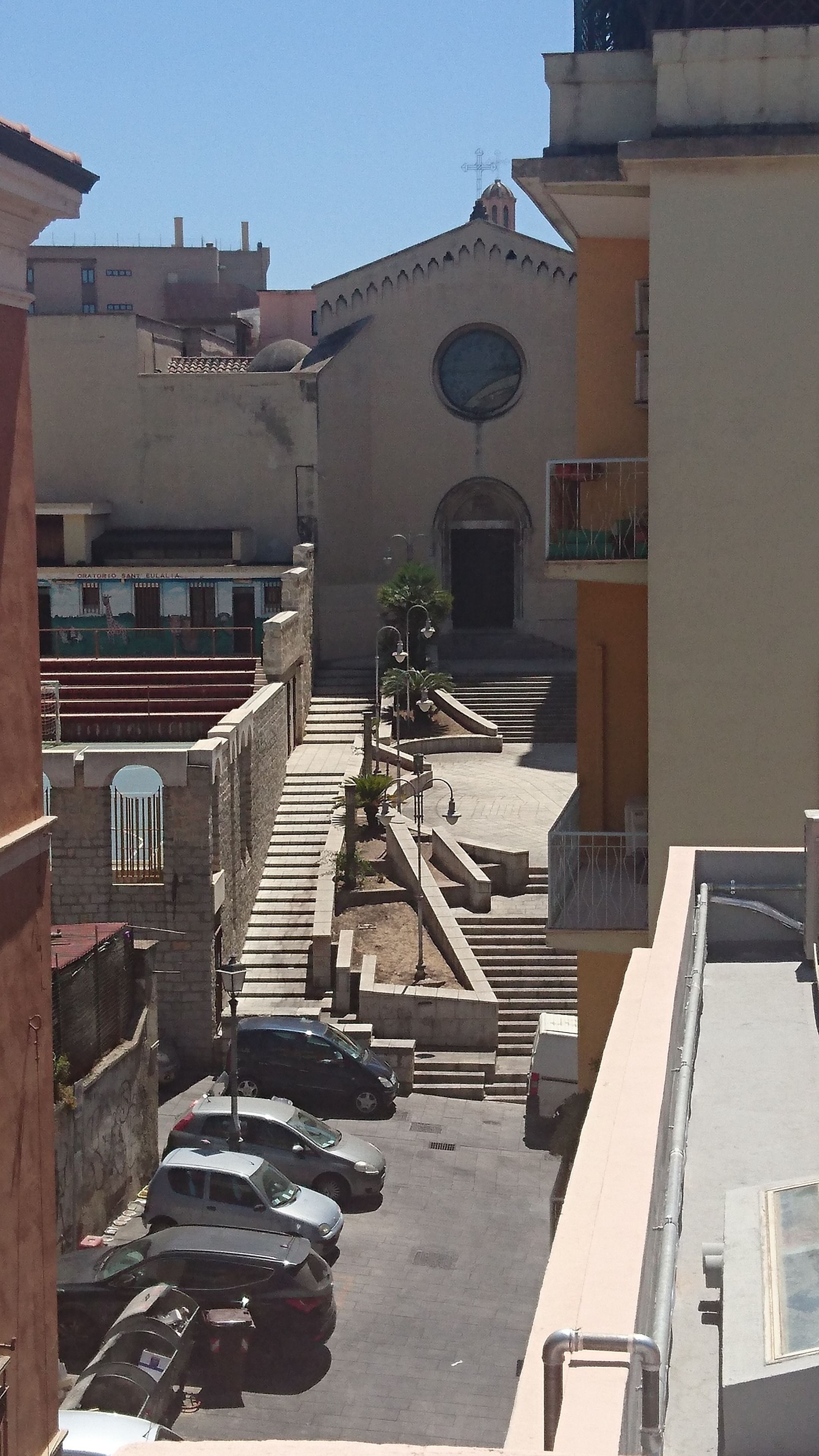 Straßenansicht mit einer Kirche, parkenden Autos und einer Treppe, die zu einem Hauseingang führt.