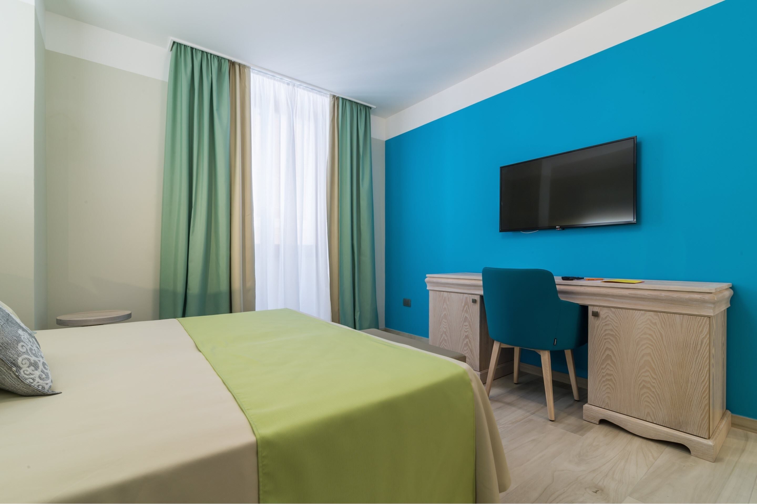 Une chambre d’hôtel équipée d’un lit, d’un bureau, d’une chaise, d’une télévision et d’une fenêtre avec des rideaux.