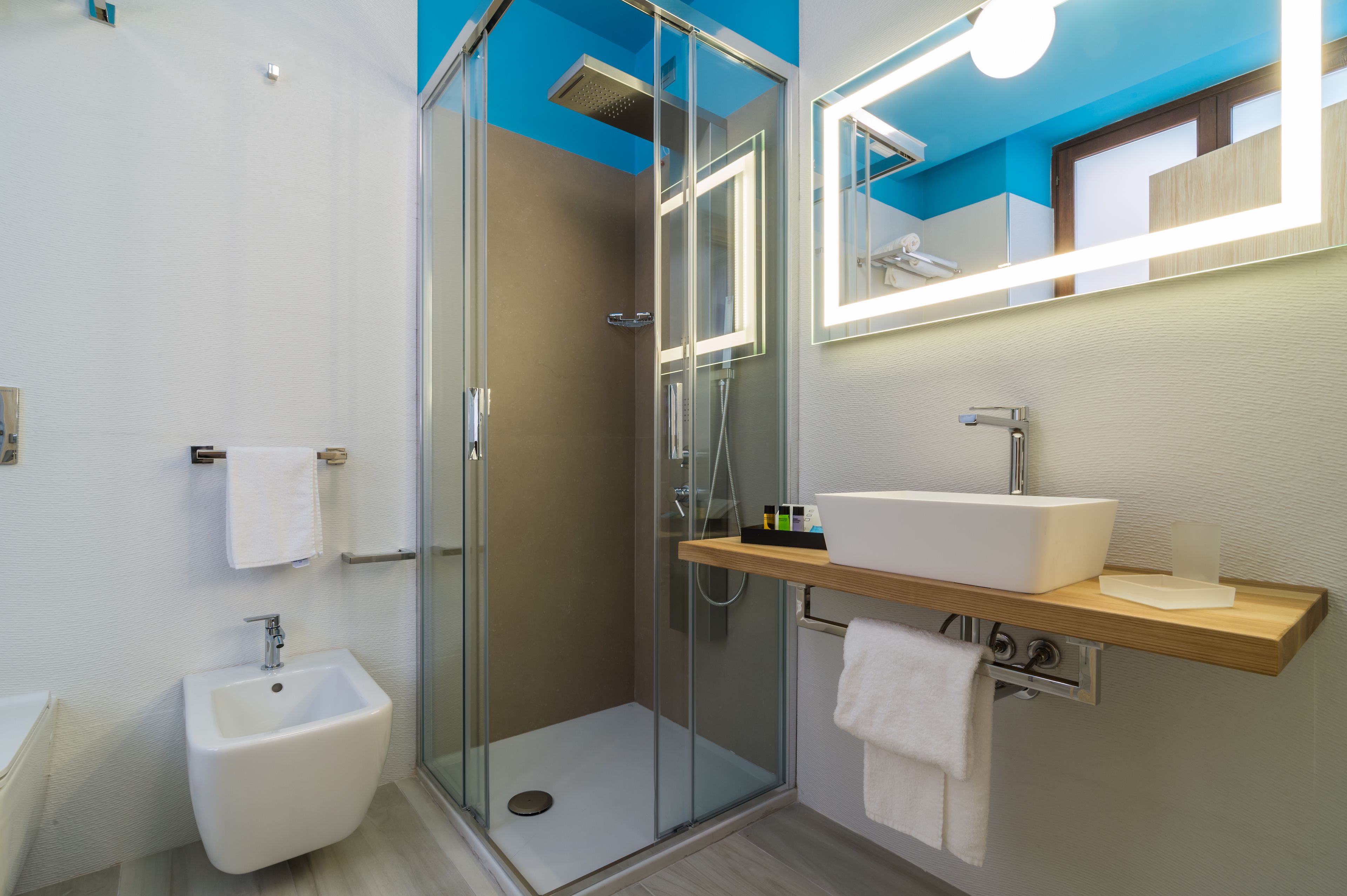Un baño moderno con ducha de vidrio, un bidé, un lavamanos con espejo y un perchero para toallas.