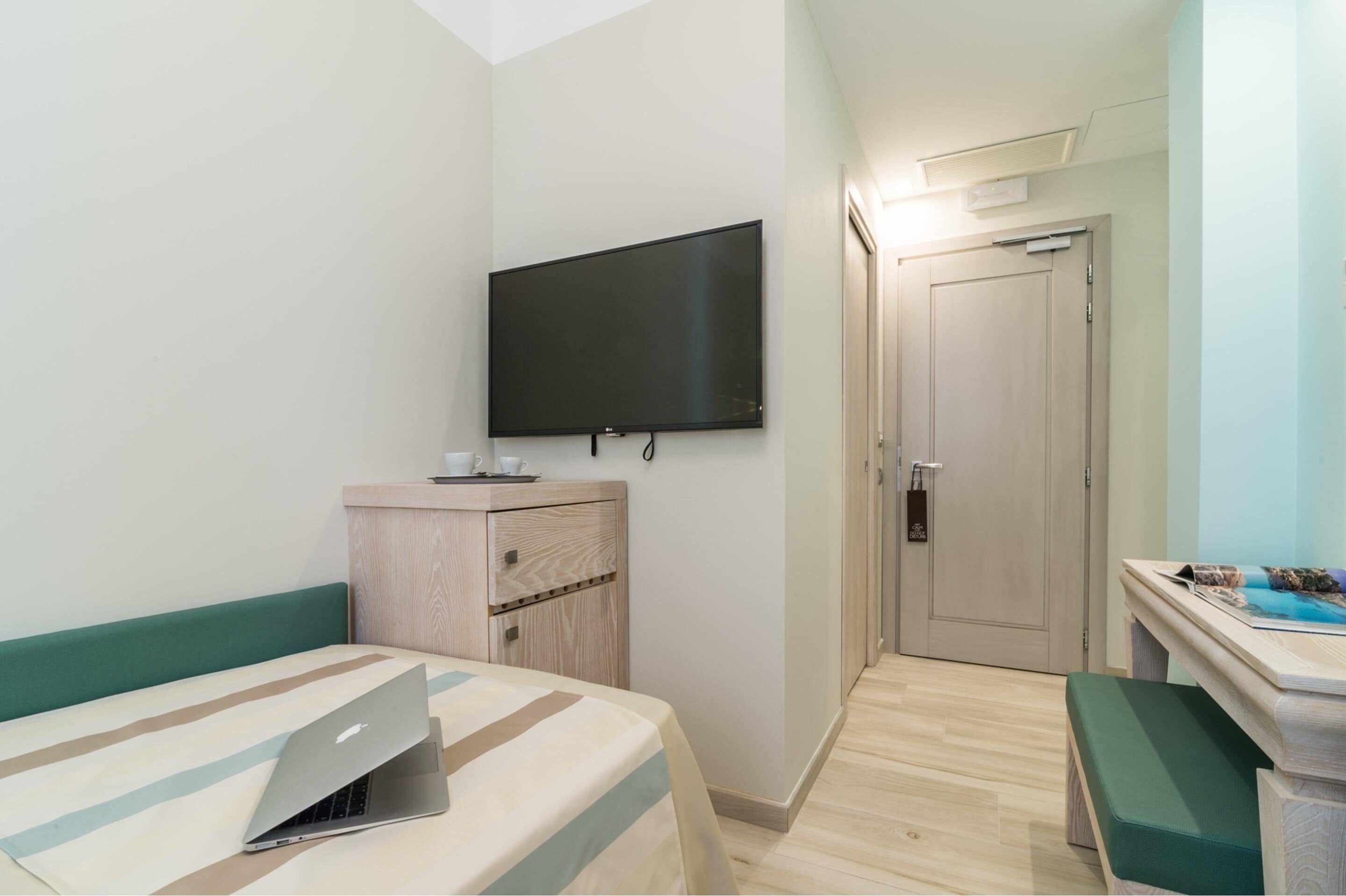 A hotel room with a bed, a desk, a television, and a door.