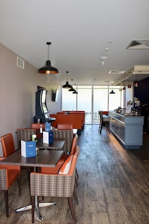 A modern dining area with wooden tables and orange chairs, a kitchen area with a bar, and large windows providing natural light. - Riverstone Lodge Hotel (Perth)