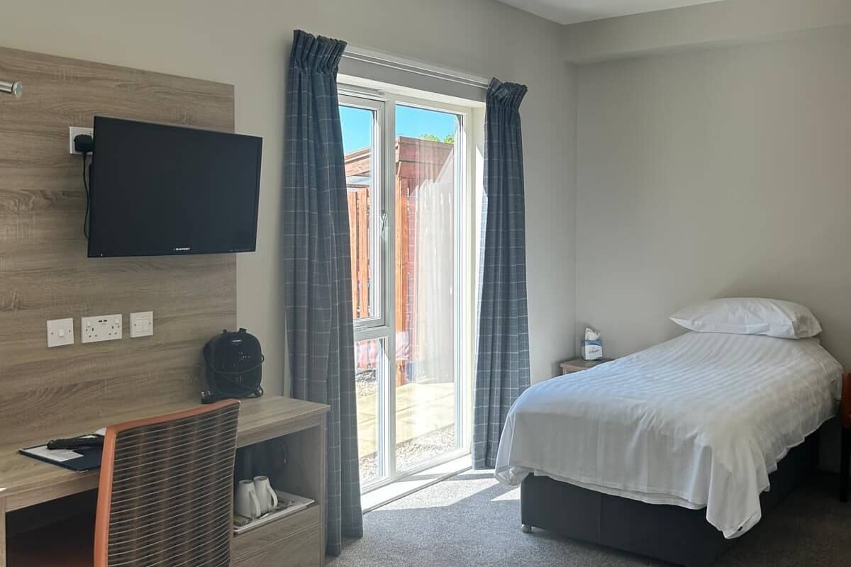 A hotel room with a desk, chair, bed, and a television mounted on the wall.