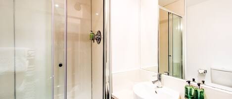 A modern bathroom with a glass-enclosed shower, a white sink, and a large mirror.