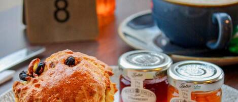 A breakfast tray with a scone, jam, butter, and a cup of coffee on a table.