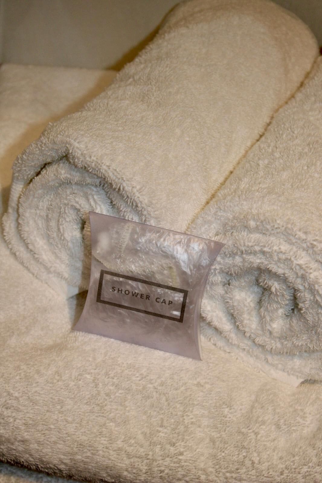 A rolled white towel with a shower cap on top.