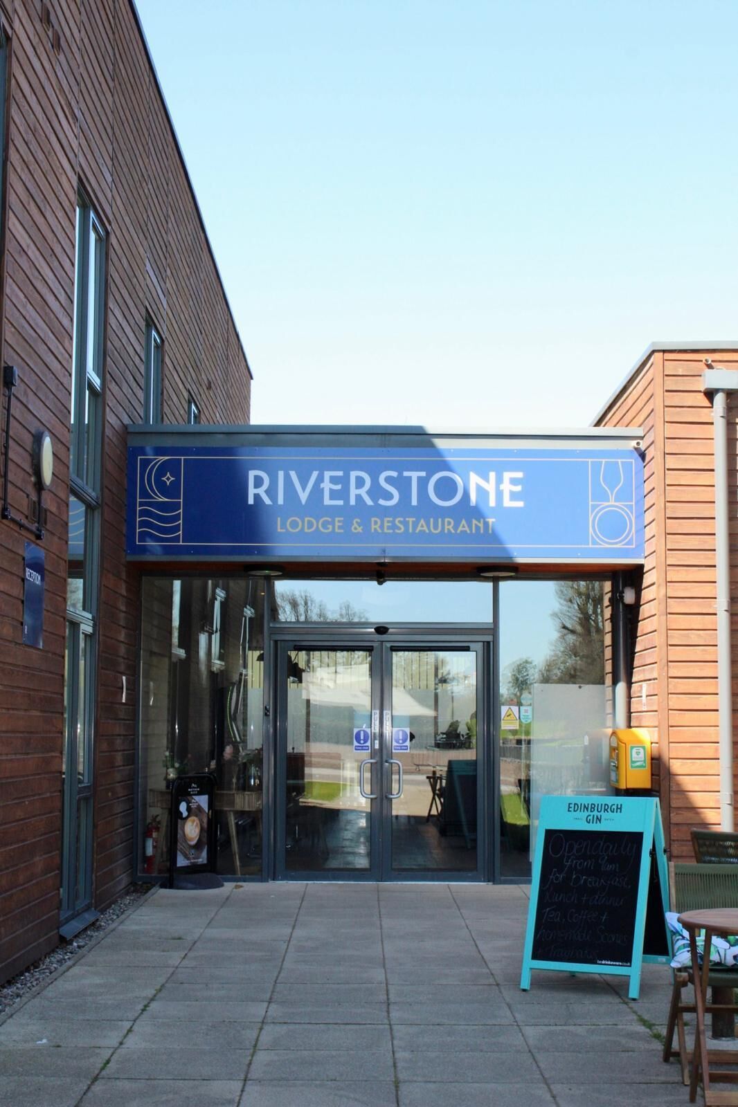 A Riverstone Lodge & Restaurant entrance with a glass door, a signboard, and a chalkboard menu outside.