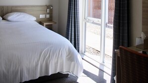 A bedroom with a bed, a nightstand, a chair, and a window with curtains. - Riverstone Lodge Hotel (Perth)