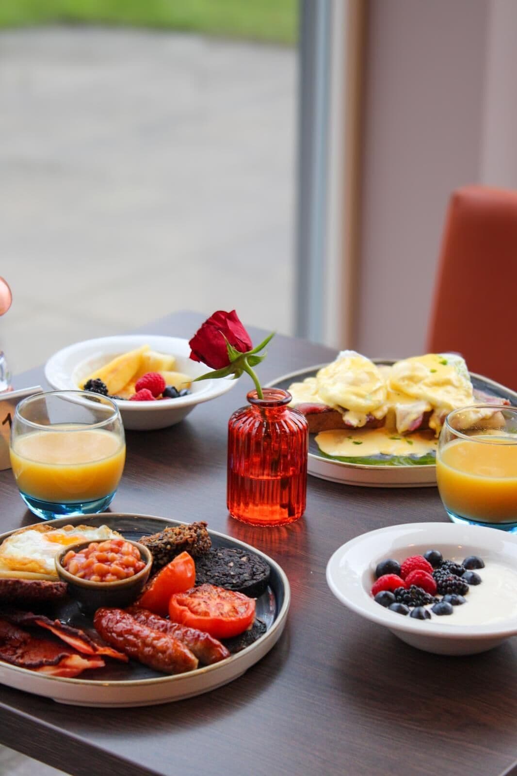 A breakfast table with plates of food, a glass of orange juice, and a red rose.