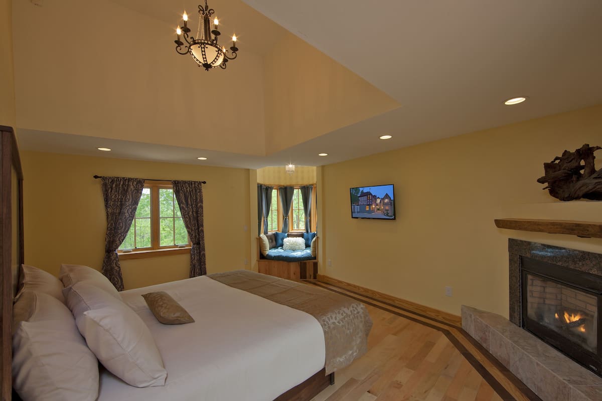 A bedroom with a large bed, a fireplace, and a television on the wall.