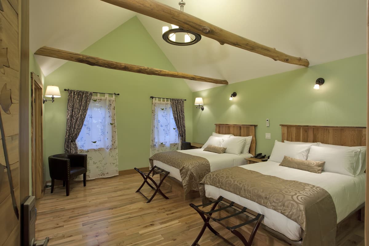 A room with two beds, wooden flooring, and a sloped ceiling with exposed beams.