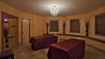Relax in a serene space with two massage tables, a chandelier, and a peaceful atmosphere.