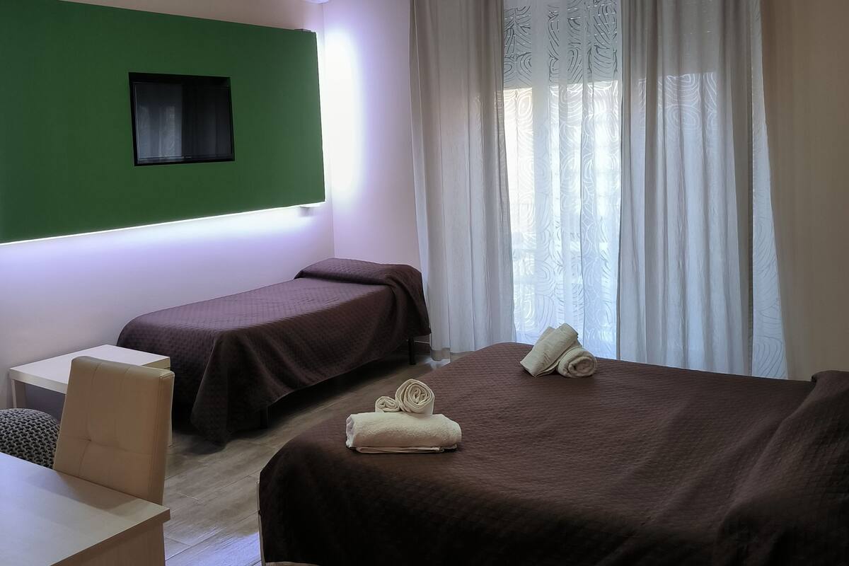 Une chambre d’hôtel avec deux lits, un bureau, une chaise et un mur d’accent vert.