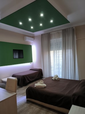 Ein Hotelzimmer mit zwei Betten, einem Schreibtisch, einem Sessel und einer Wand in Grüntönen.