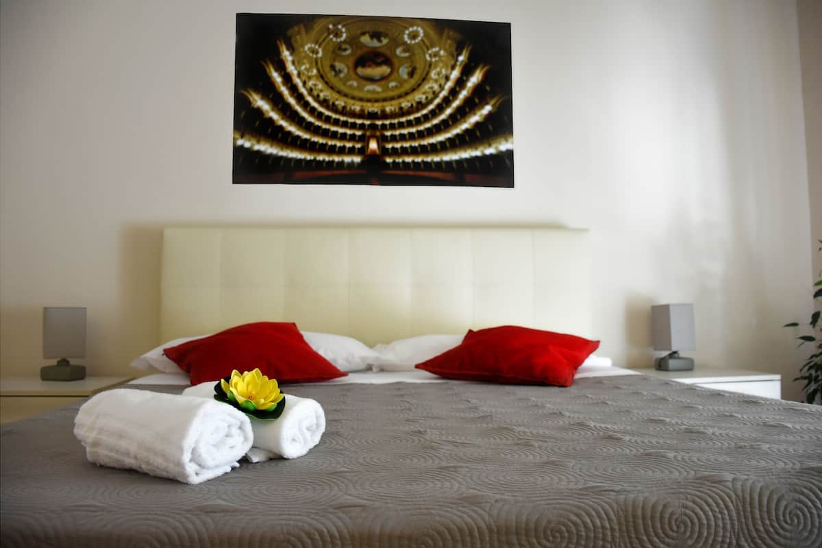 Un lit bien fait, avec des oreillers rouges et blancs, une serviette blanche pliée et une fleur jaune posée sur le lit.