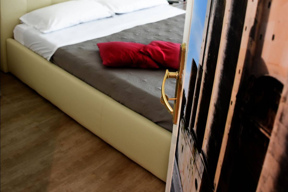 Un lit avec une tête de lit, un oreiller rouge et un tableau accroché au mur.