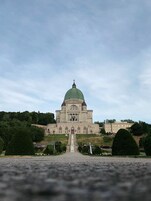 Un grand bâtiment historique, doté d’un dôme imposant et surmonté d’une croix, entouré de verdure et accessible par un chemin pavé menant à l’entrée.