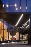 The exterior of Hotel Mon Vieux Montreal with large glass windows, a modern facade, and illuminated signage.