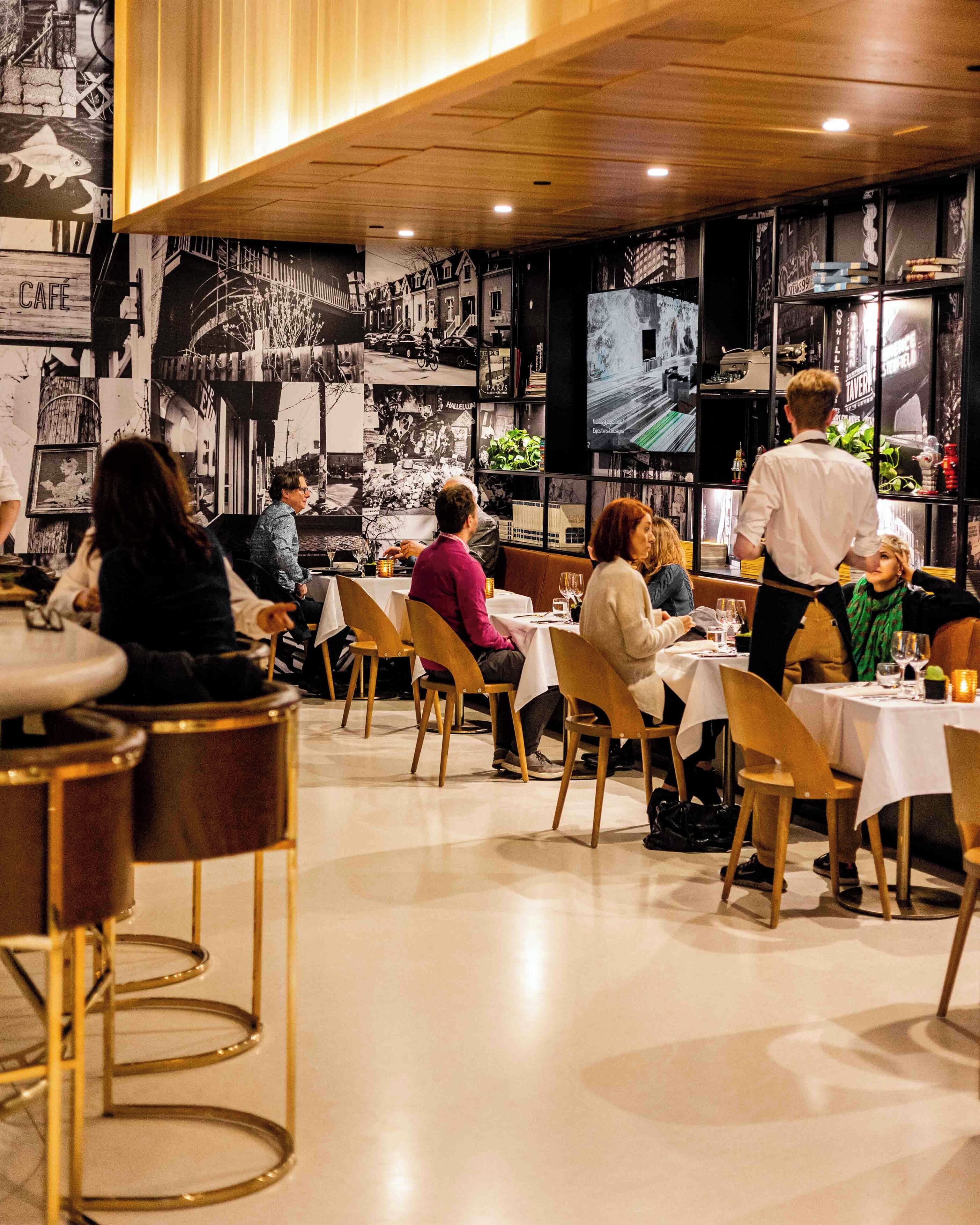 Un restaurante con mesas y sillas, un camarero y una pared con fotografías en blanco y negro.