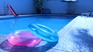 Una piscina con flotadores, tobogán y un banco.