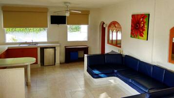 A compact living space with a kitchenette, a dining area, a sofa, and a television mounted on the wall.