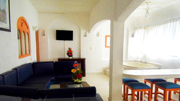 Una sala de estar con un sofá, una mesa de centro con flores, un televisor de pantalla plana y un comedor con sillas y una mesa.