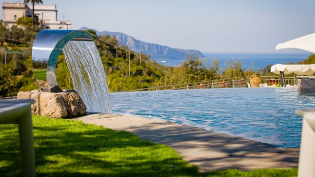 Piscina con cascada, rodeada de follaje y vistas a montañas.