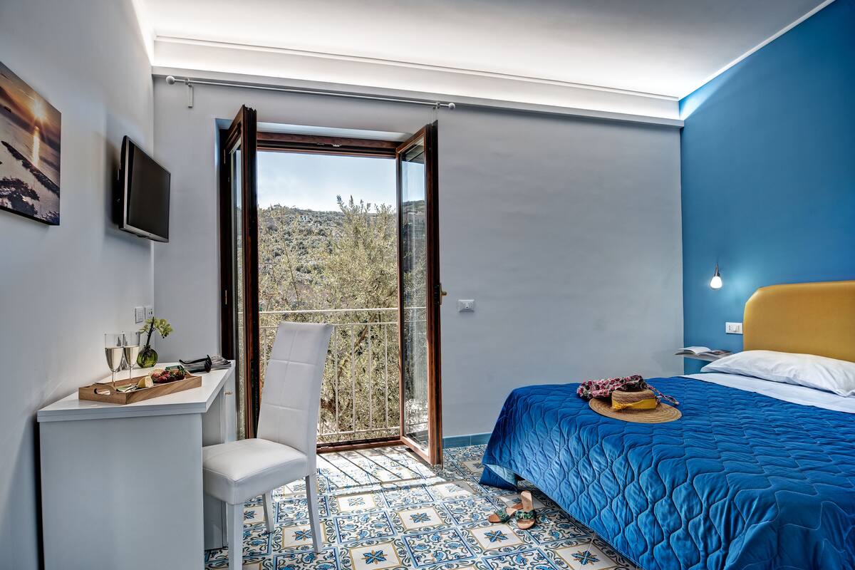 Een slaapkamer met een bed, een bureau, een stoel en een groot raam.