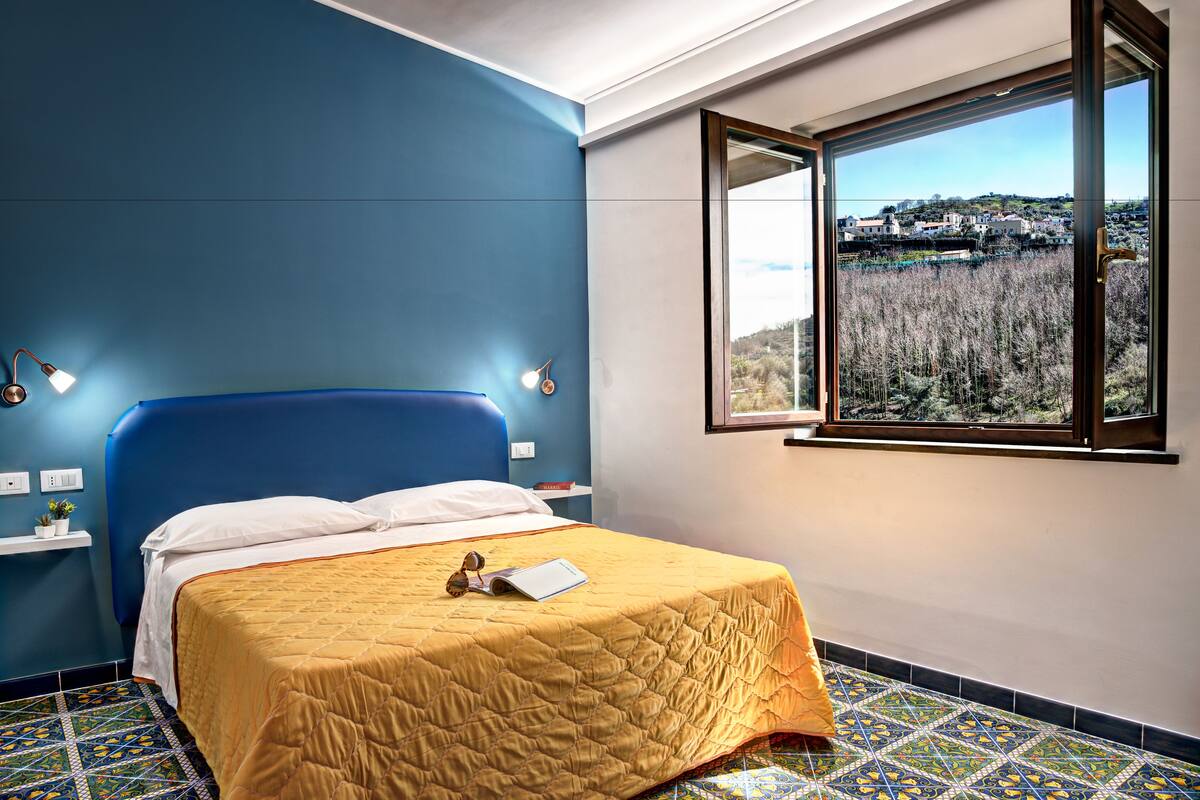 Een slaapkamer met een bed, een raam met uitzicht en een blauwe muur.