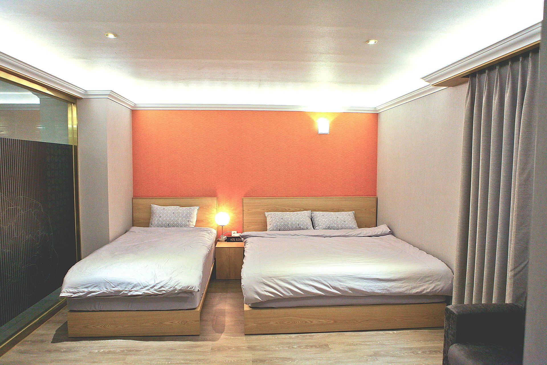 Une chambre d’hôtel avec deux lits, une table de chevet, une lampe fixée au mur et une fenêtre avec des rideaux.