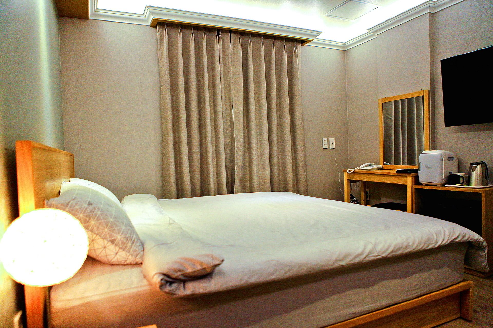 Una habitación de hotel con cama, mesita de noche con lámpara, teléfono y cafetera.