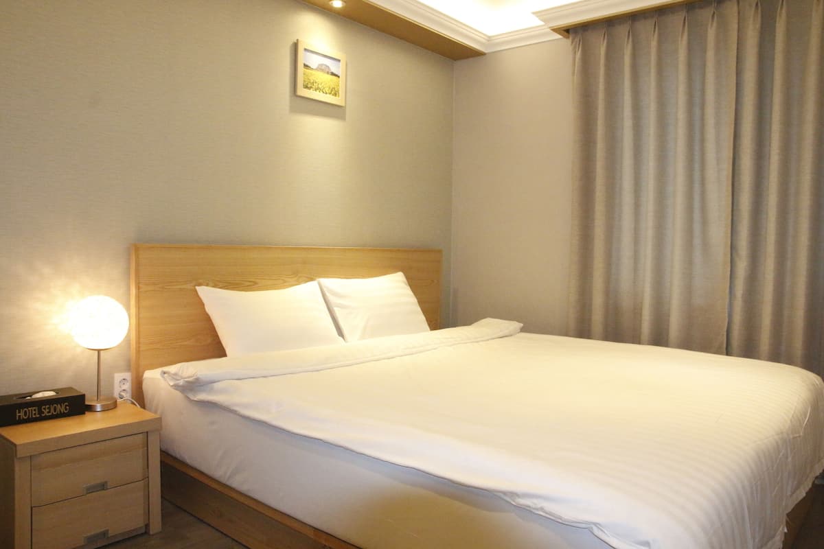 Ein Hotelzimmer mit einem ordentlich bezogenen Bett, einem Nachttisch mit Lampe und einem gerahmten Bild an der Wand.